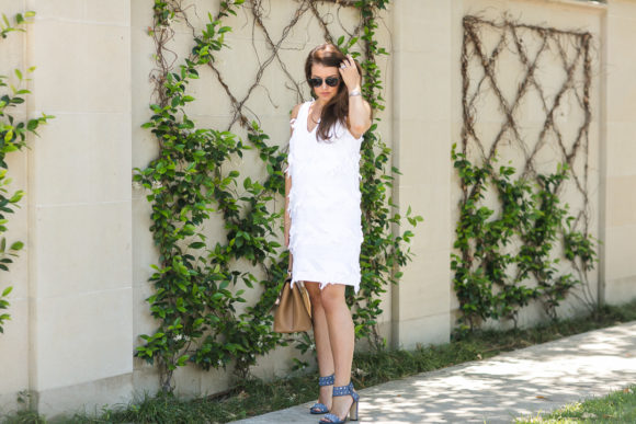 Amy Havins wears a white shift dress and neutral sandals.