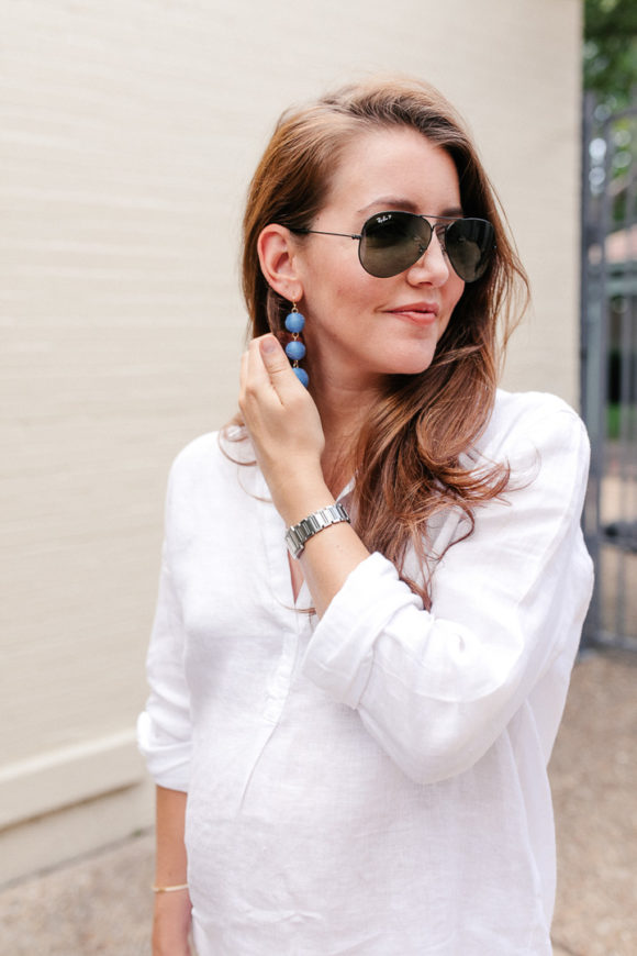 Amy Havins wears white jeans and a white blouse with statement earrings.
