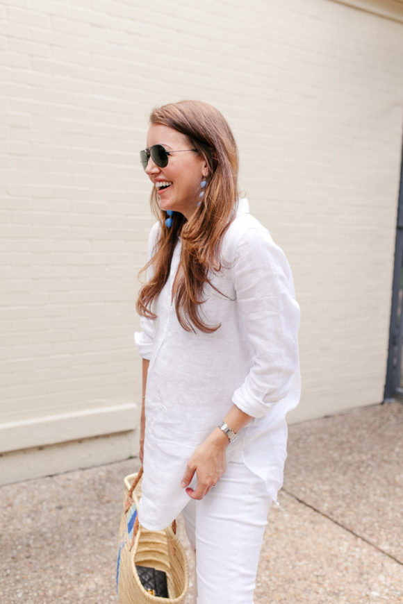 Amy Havins wears white jeans and a white blouse with statement earrings.