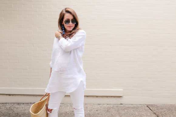 Amy Havins wears white jeans and a white blouse with statement earrings.