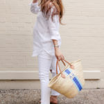 Amy Havins wears white jeans and a white blouse with statement earrings.