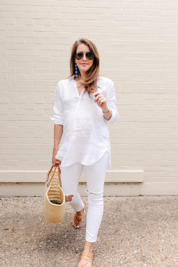 Amy Havins wears white jeans and a white blouse with statement earrings.