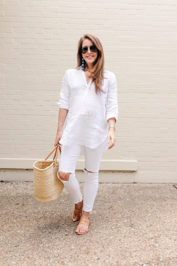 Amy Havins wears white jeans and a white blouse with statement earrings.