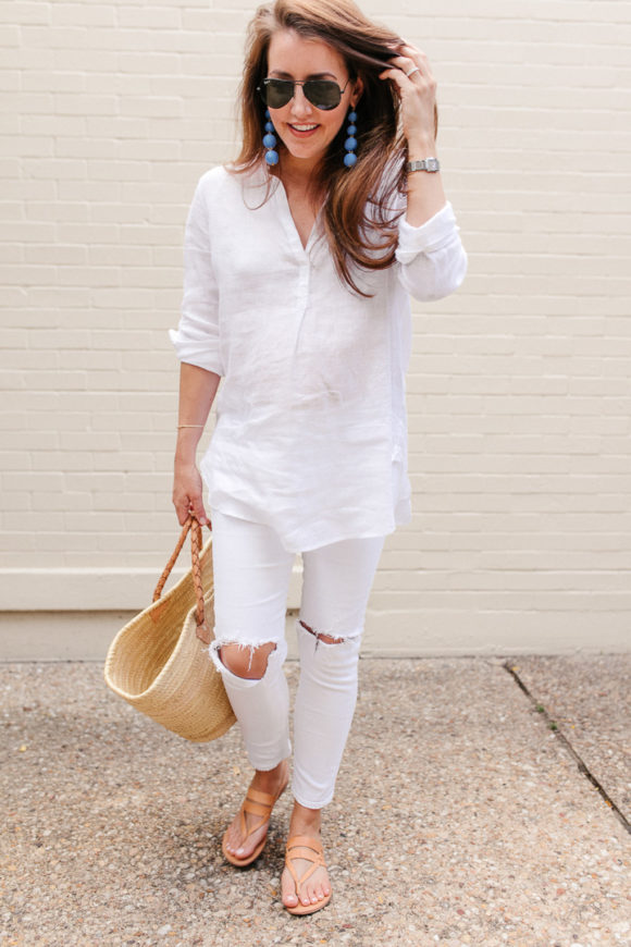 Amy Havins wears white jeans and a white blouse with statement earrings.