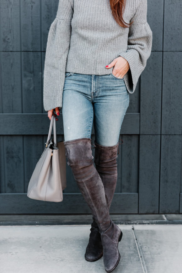 Amy havins wears a gray sweater and over the knee boots.