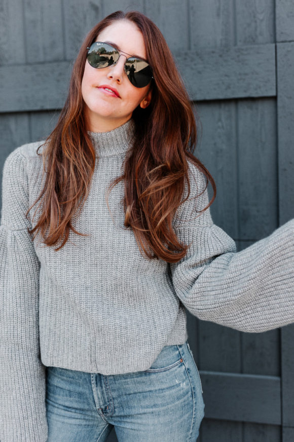 Amy havins wears a gray sweater and over the knee boots.