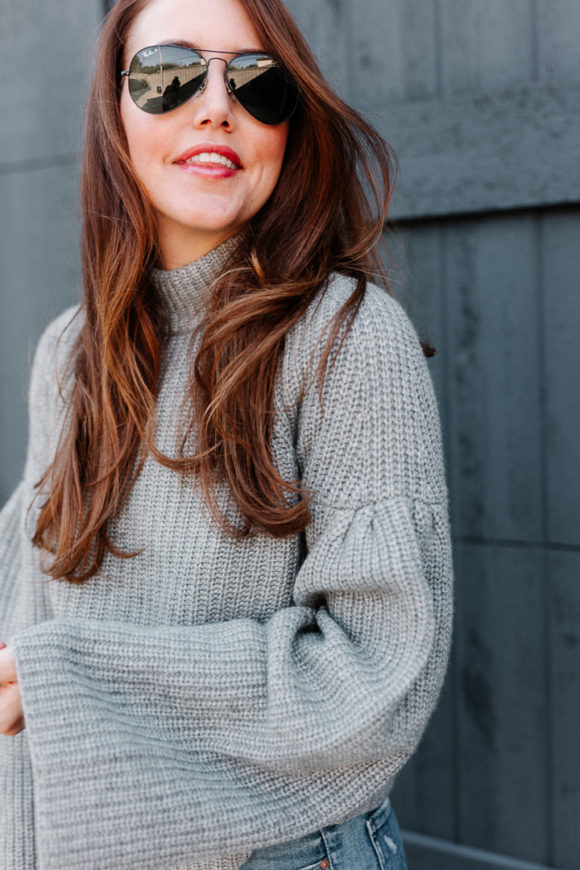 Amy havins wears a gray sweater and over the knee boots.