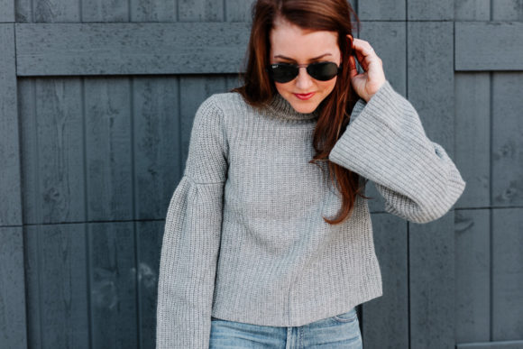 Amy havins wears a gray sweater and over the knee boots.