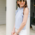 Amy Havins wears white jeans and a sleeveless ruffle blouse.