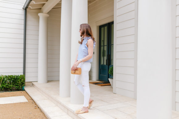 Amy Havins wears white jeans and a sleeveless ruffle blouse.