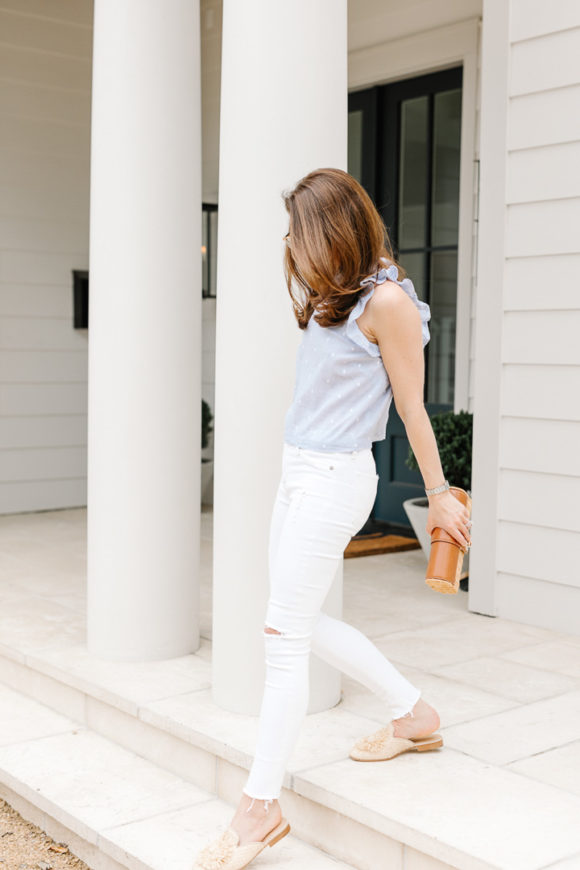 Amy Havins wears white jeans and a sleeveless ruffle blouse.