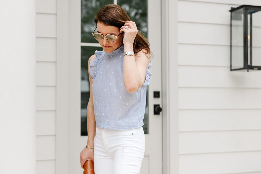 Amy Havins wears white jeans and a sleeveless ruffle blouse.