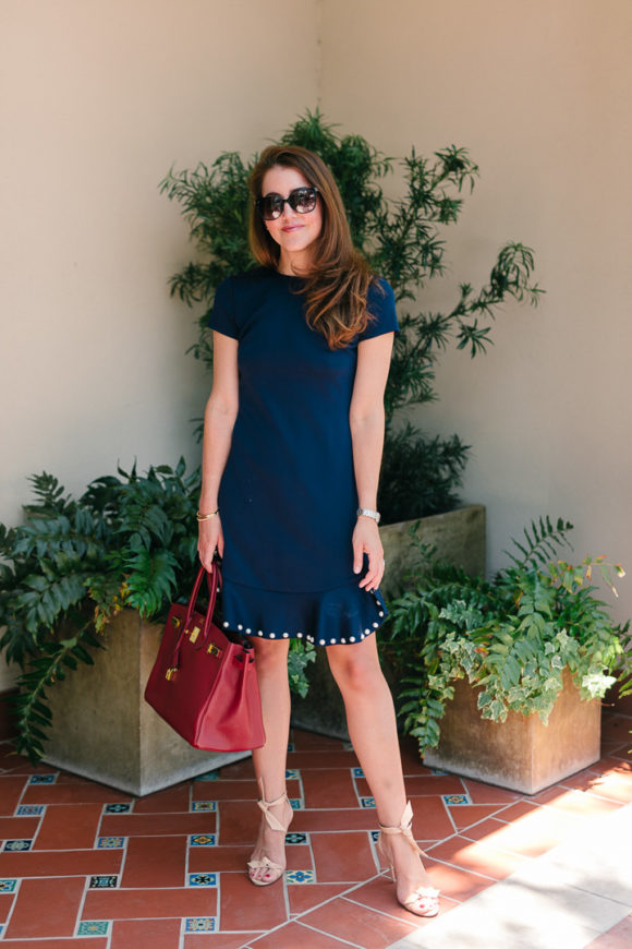 Amy havins wears a navy shift dress with pearl details.