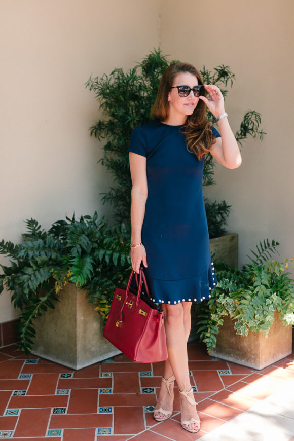 Amy havins wears a navy shift dress with pearl details.